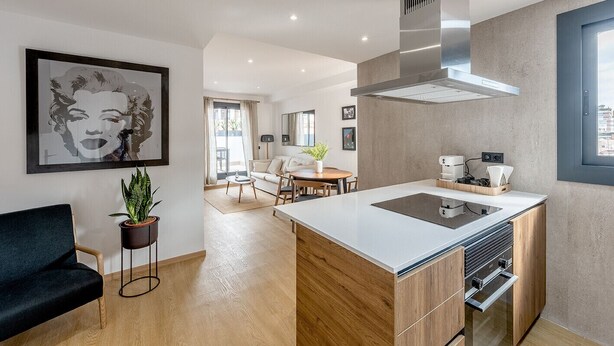 A modern kitchen with a central island, a dining area with a sofa and table, and a living room with a sofa and a plant. - GA1 (Barcelona)
