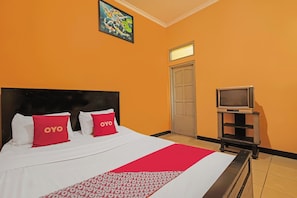 Una habitación de hotel con una cama, dos almohadas rojas con el texto "OYO", un televisor sobre un soporte y una puerta con un ventanal.