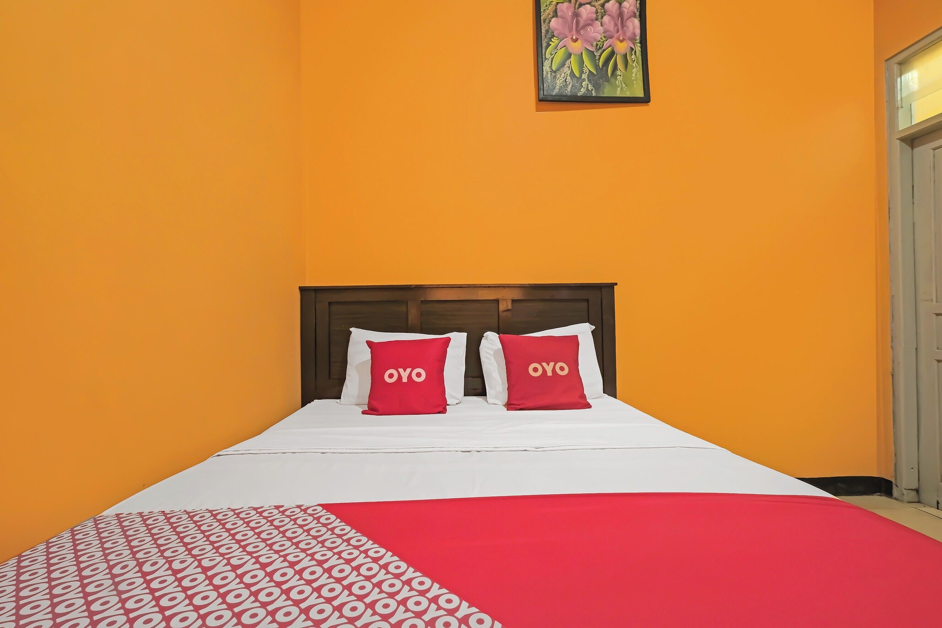 Una cama con una colcha blanca y roja estampada, dos almohadas rojas con la palabra "OYO" y un cabecero de madera.