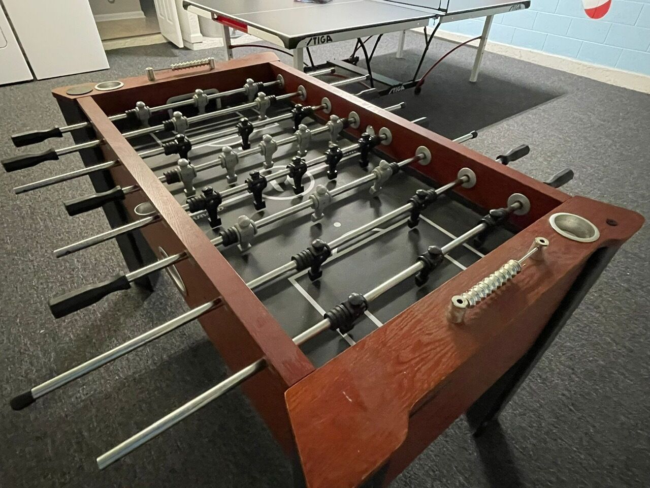 A foosball table with a wooden frame and metal rods, placed on a carpeted floor.