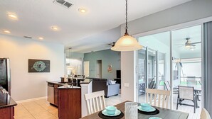 Una cocina moderna con comedor, que presenta un tavolo de madera con cuencos y platos azules, una lámpara colgante y vistas al jardín trasero a través de grandes puertas corredizas de vidrio.