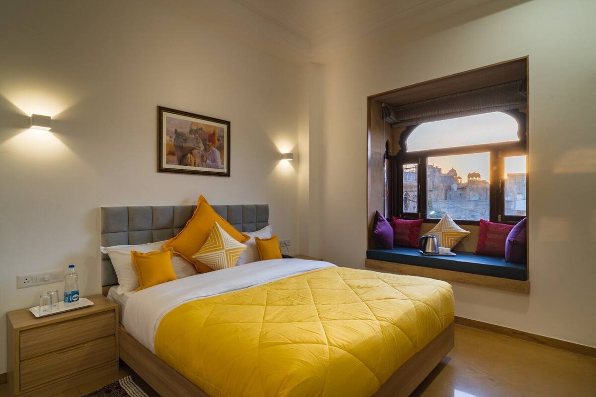 Quarto de hotel com cama, mesa de cabeceira e janela com vista para a paisagem urbana.