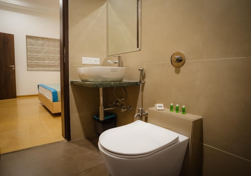 Et moderne badeværelse med et hvidt toilet, en væghængt vask og et håndholdt brusehoved.