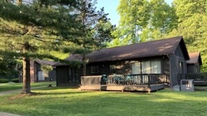 A cabin with a porch, surrounded by trees and a well-maintained lawn.