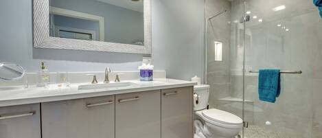 A modern bathroom with a large mirror, a glass shower enclosure, and a white sink.