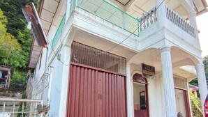 Uma casa de dois andares com varanda, um grande portão vermelho e uma placa com a inscrição 'Villa'.