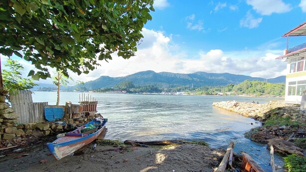 Vista ribeirinha com barcos, um muro de pedra e um edifício com varanda.