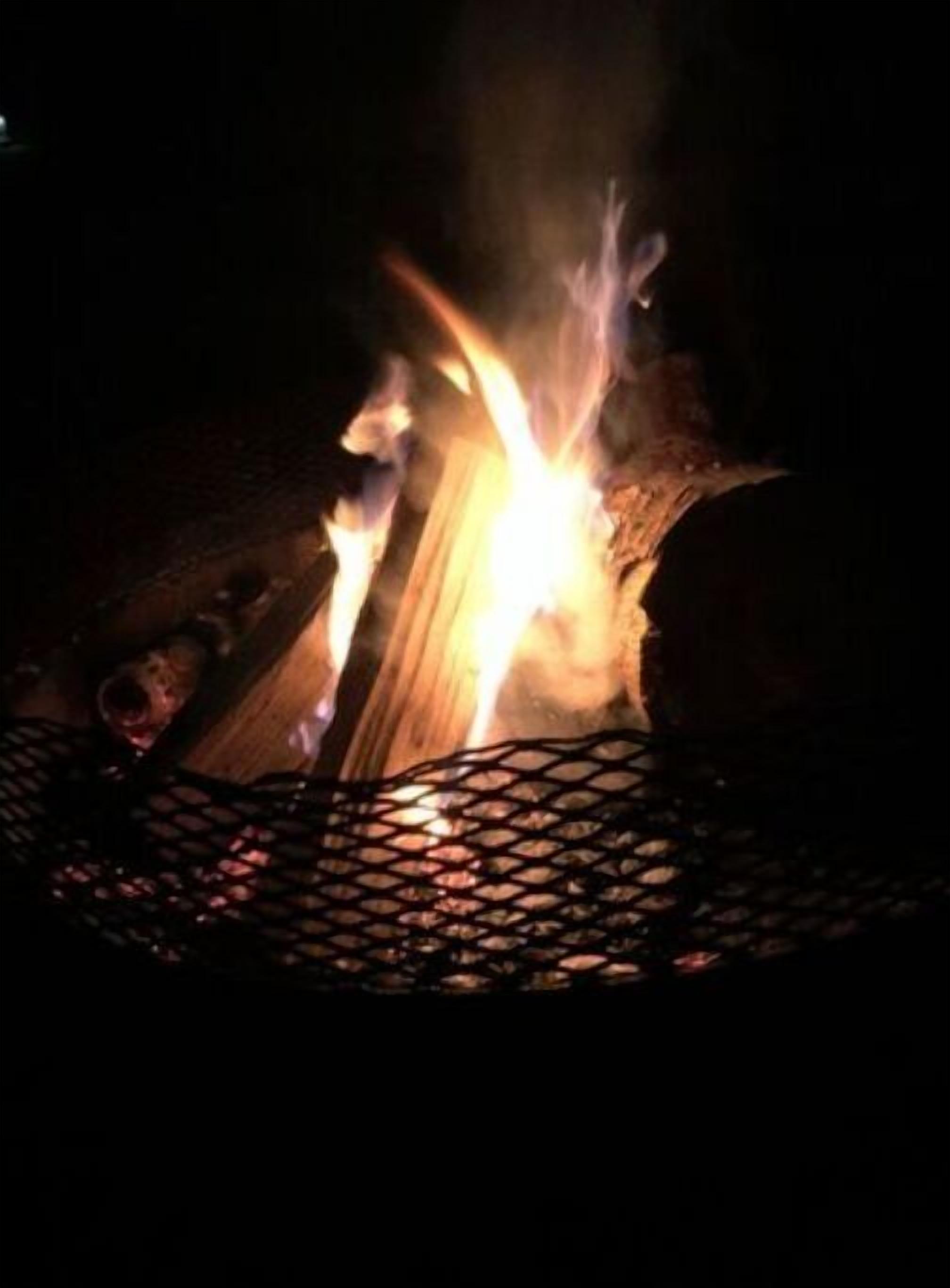 Ein Lagerfeuer mit Holzscheiten und einem Drahtkorb-Feuerkorb.