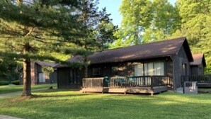 Un chalet rustique doté d’une véranda, entouré d’une pelouse bien entretenue et d’arbres.