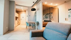 Un salon moderne avec un canapé gris, un coin repas avec une table et des chaises, et une cuisine en arrière-plan.