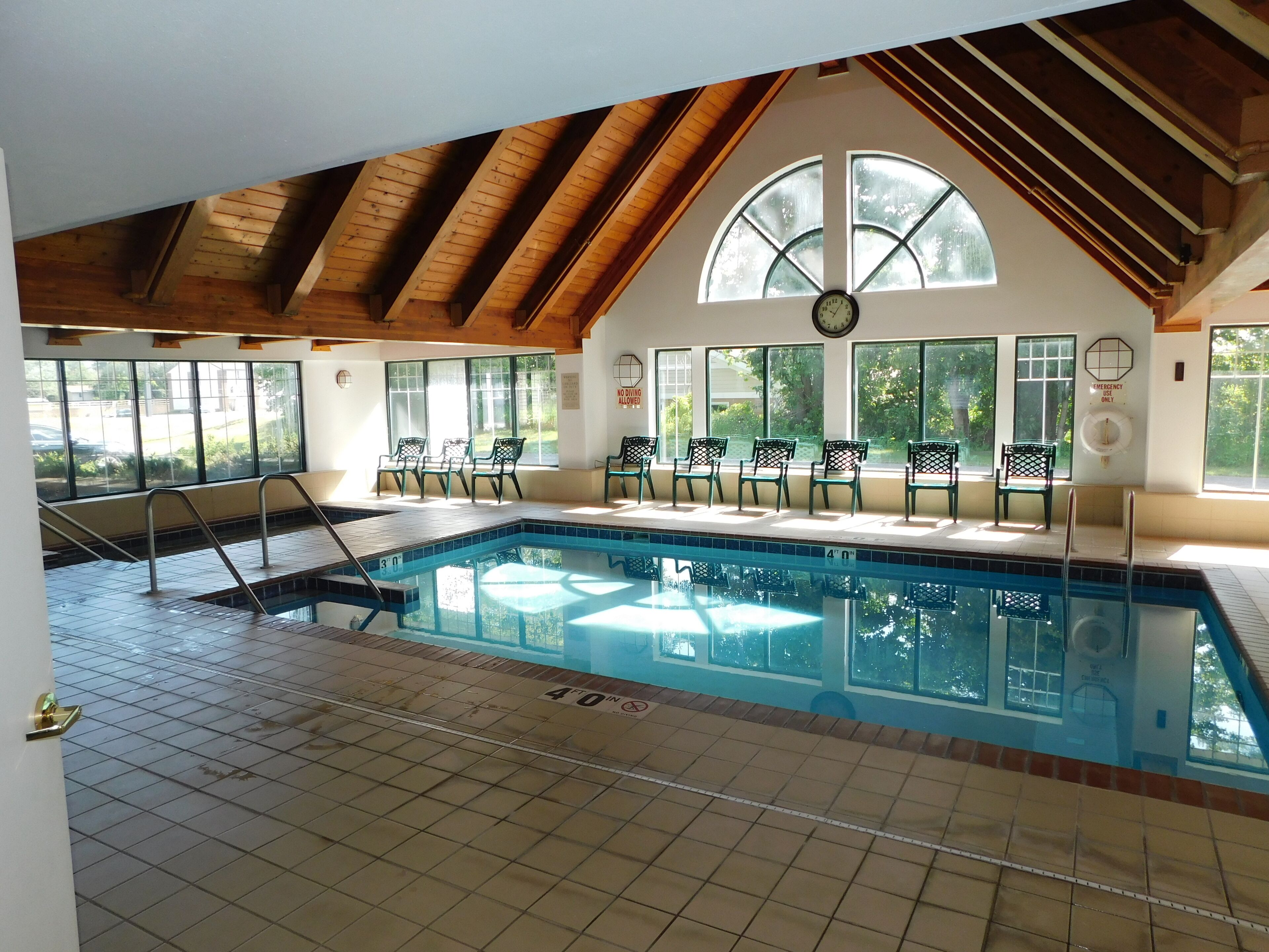 An indoor swimming pool with a tiled floor, a wooden ceiling, and large windows.