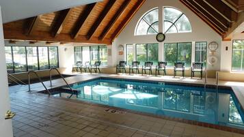 An indoor swimming pool with a tiled floor, a wooden ceiling, and large windows.
