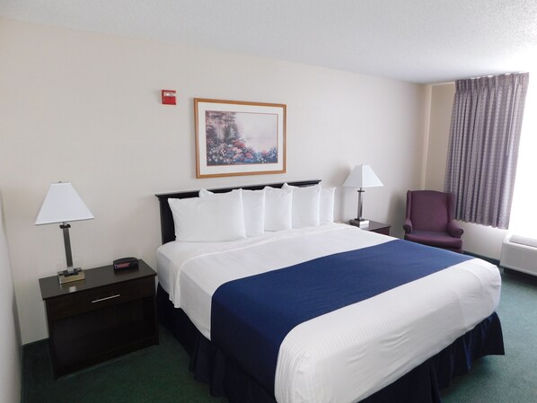 A hotel room with a large bed, two bedside tables, a chair, a window with curtains, and a framed picture on the wall.