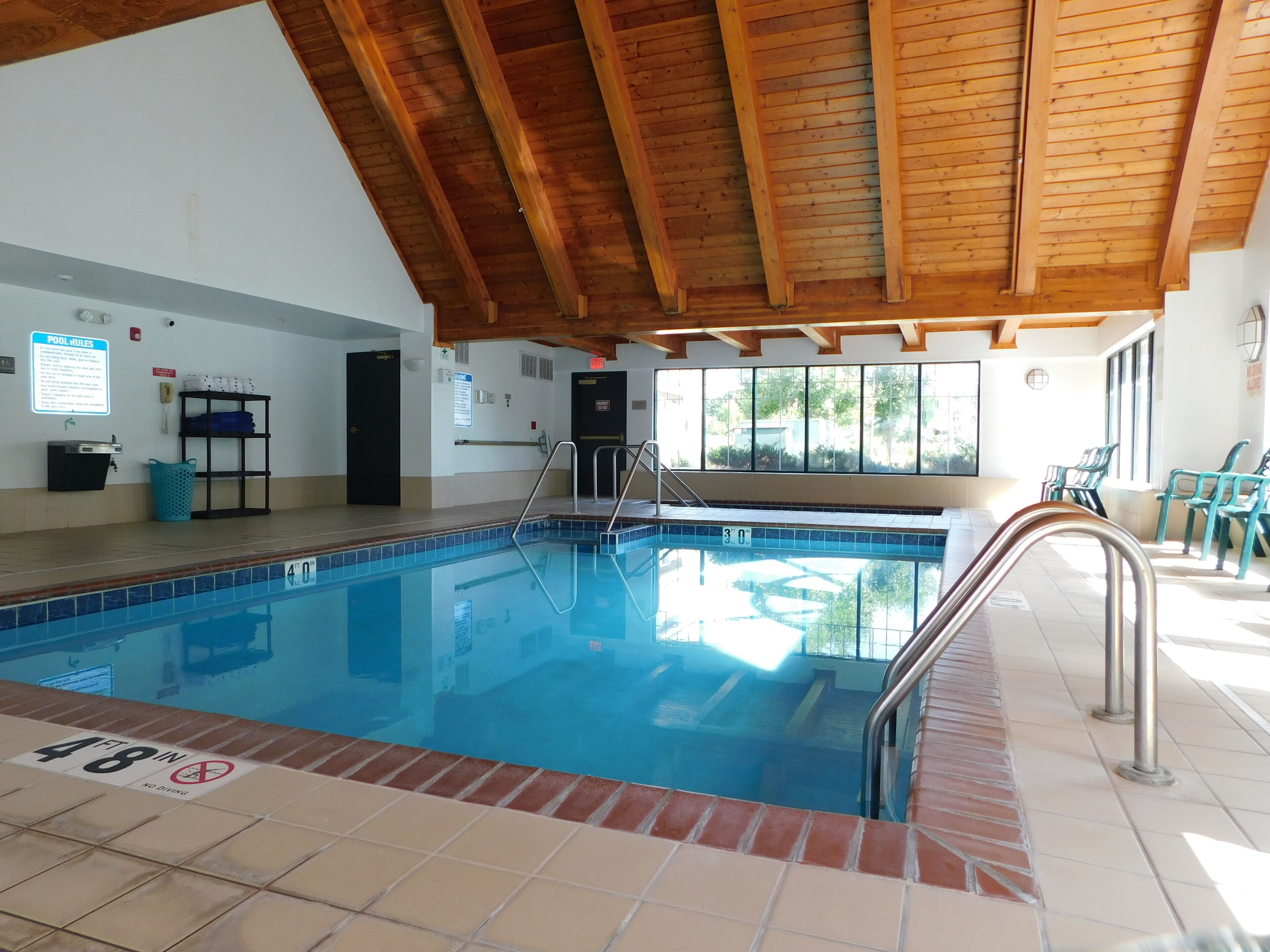Una piscina interior con techo de madera, un cartel con las normas de la piscina y vistas al exterior a través de amplios ventanales.