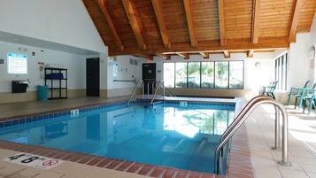 Una piscina interior con techo de madera, un cartel con las normas de la piscina y vistas al exterior a través de amplios ventanales.