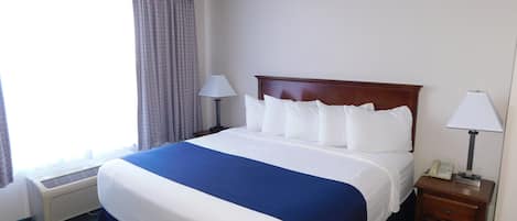 Habitación de hotel con una cama grande, dos mesitas de noche con lámparas, un teléfono y una ventana con cortinas.