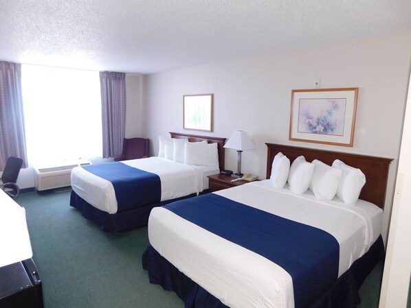 A hotel room with two beds, a desk, a chair, a lamp, and a painting on the wall.