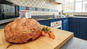 A kitchen with a large loaf of bread on a wooden cutting board, a tomato plant, and blue cabinets. - Spindrift (Weymouth)