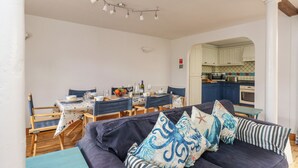 A cozy living room with a dark blue sofa, striped pillows, and a dining area with wooden chairs and a table set for two. - Spindrift (Weymouth)
