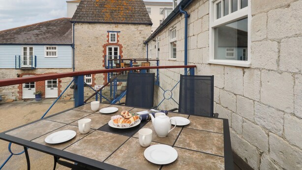 A rooftop terrace with a table set for a meal, a brick chimney, and a view of neighboring buildings. - Spindrift (Weymouth)