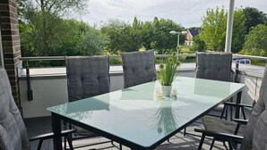 A glass-top table with four chairs, a potted plant, and a clear view of the surrounding greenery and buildings. - Park - Apartment 10 im Marinapark Scharmützelsee, Sauna, Kamin, 6 Pers., 89 m² (Wendisch Rietz Siedlung)