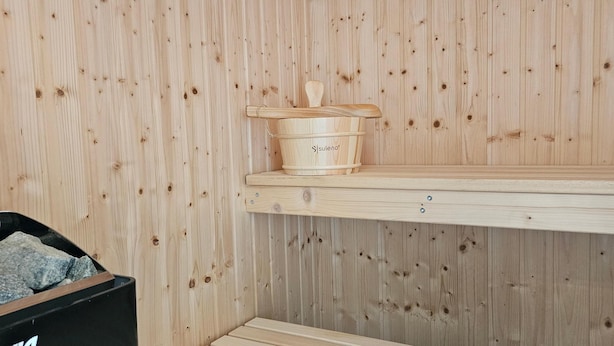 A wooden sauna with a wooden bench, a small shelf with a pot, and a trash bin with rocks. - Park - Apartment 10 im Marinapark Scharmützelsee, Sauna, Kamin, 6 Pers., 89 m² (Wendisch Rietz Siedlung)