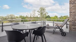 A balcony with a round table and chairs, a sun lounger, and a view of trees and buildings. - Park - Apartment 12 im Marinapark Scharmützelsee, Sauna, Whirlpool, E - Kamin, 4 Pers., 80 m² (Wendisch Rietz Siedlung)