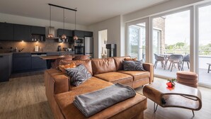 A modern kitchen with dark cabinets and stainless steel appliances, a brown leather sofa with cushions, and a wooden coffee table. - Park - Apartment 12 im Marinapark Scharmützelsee, Sauna, Whirlpool, E - Kamin, 4 Pers., 80 m² (Wendisch Rietz Siedlung)