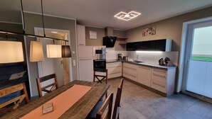 A modern kitchen with white cabinets, a built-in oven, and a coffee maker. There is a dining area with a wooden table and chairs. - Park - Apartment 01 im Marinapark Scharmützelsee, Sauna, Whirlpool, 6 Pers., 98 m² (Wendisch Rietz Siedlung)