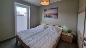 A bedroom with a bed, bedside table, nightstand, and a painting of a beach scene. - Park - Apartment 01 im Marinapark Scharmützelsee, Sauna, Whirlpool, 6 Pers., 98 m² (Wendisch Rietz Siedlung)