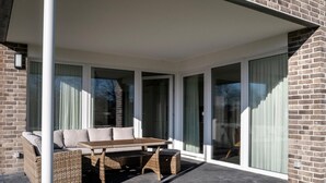 Un espacio de estar techado al aire libre con mobiliario de mimbre, grandes puertas correderas de vidrio y fachada de ladrillo.