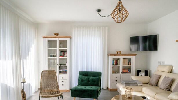 Una sala de estar moderna con un sillón verde, un sofá beige, una mesa de centro de mimbre y una estantería.