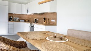 Una cocina moderna con armarios blancos, encimera de madera y comedor con mesa de madera y protectores de mesa tejidos.