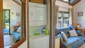 A cozy room with a grey sofa, a small table with a lamp, and a white appliance. - Mayfield Tiny Home w/ Porch, Walk to Beaches! (Mayfield)