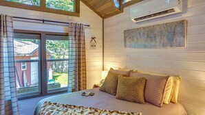 A bedroom with a bed, a window with curtains, an air conditioning unit, and a painting on the wall. - Mayfield Tiny Home w/ Porch, Walk to Beaches! (Mayfield)