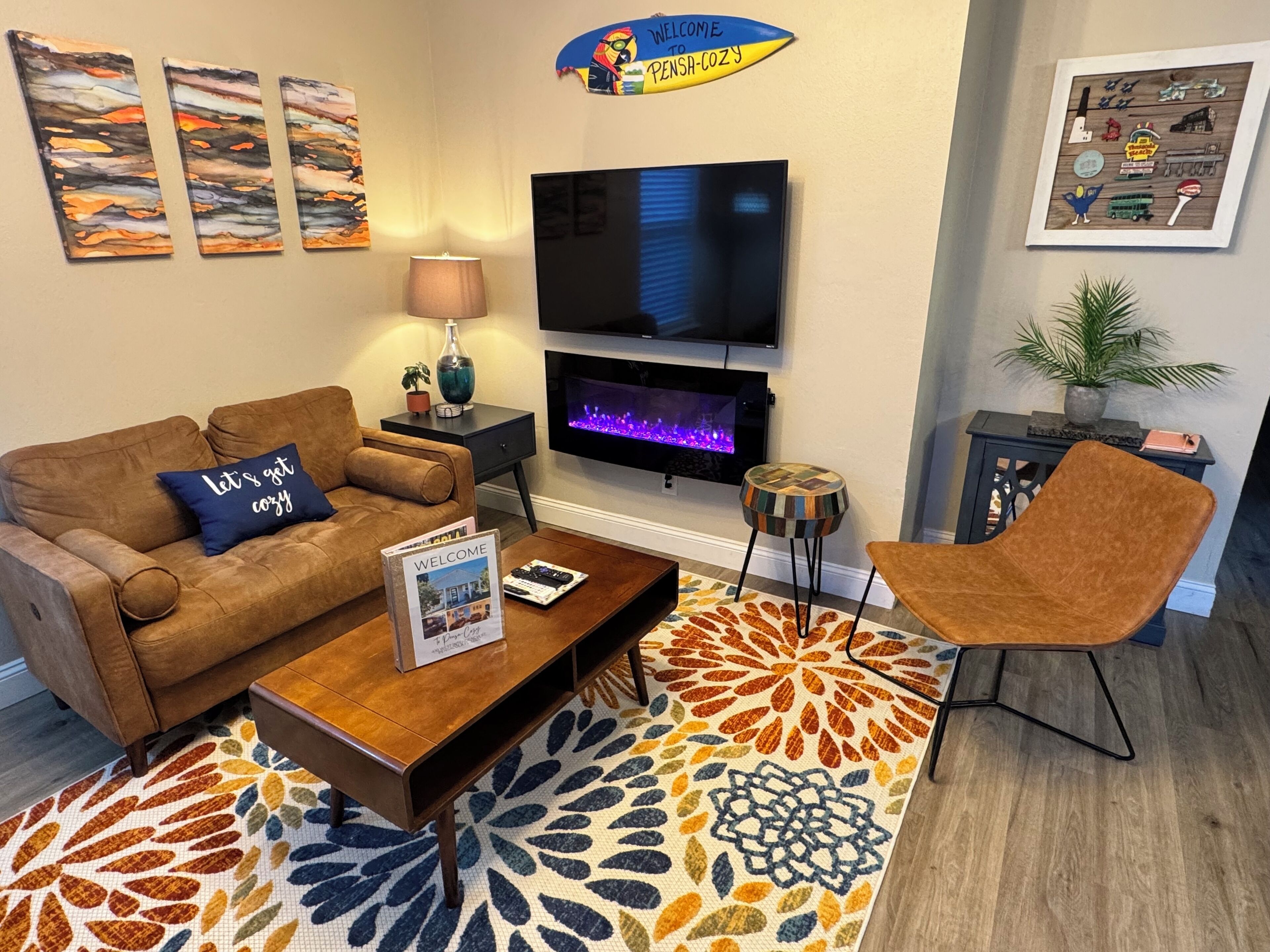 Una sala de estar acogedora con sofá, sillón, mesa de centro, televisor, chimenea y decoración mural.