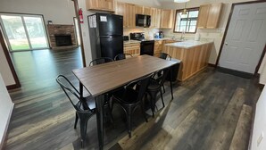 Een moderne keuken met houten kastjes, een zwarte koelkast en een eethoek met een houten tafel en zwarte stoelen.
