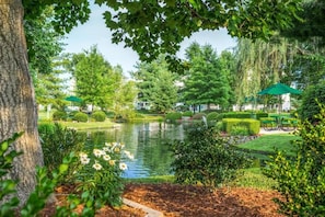 Un jardin paisible avec un étang, des haies soigneusement taillées et des parasols verts.