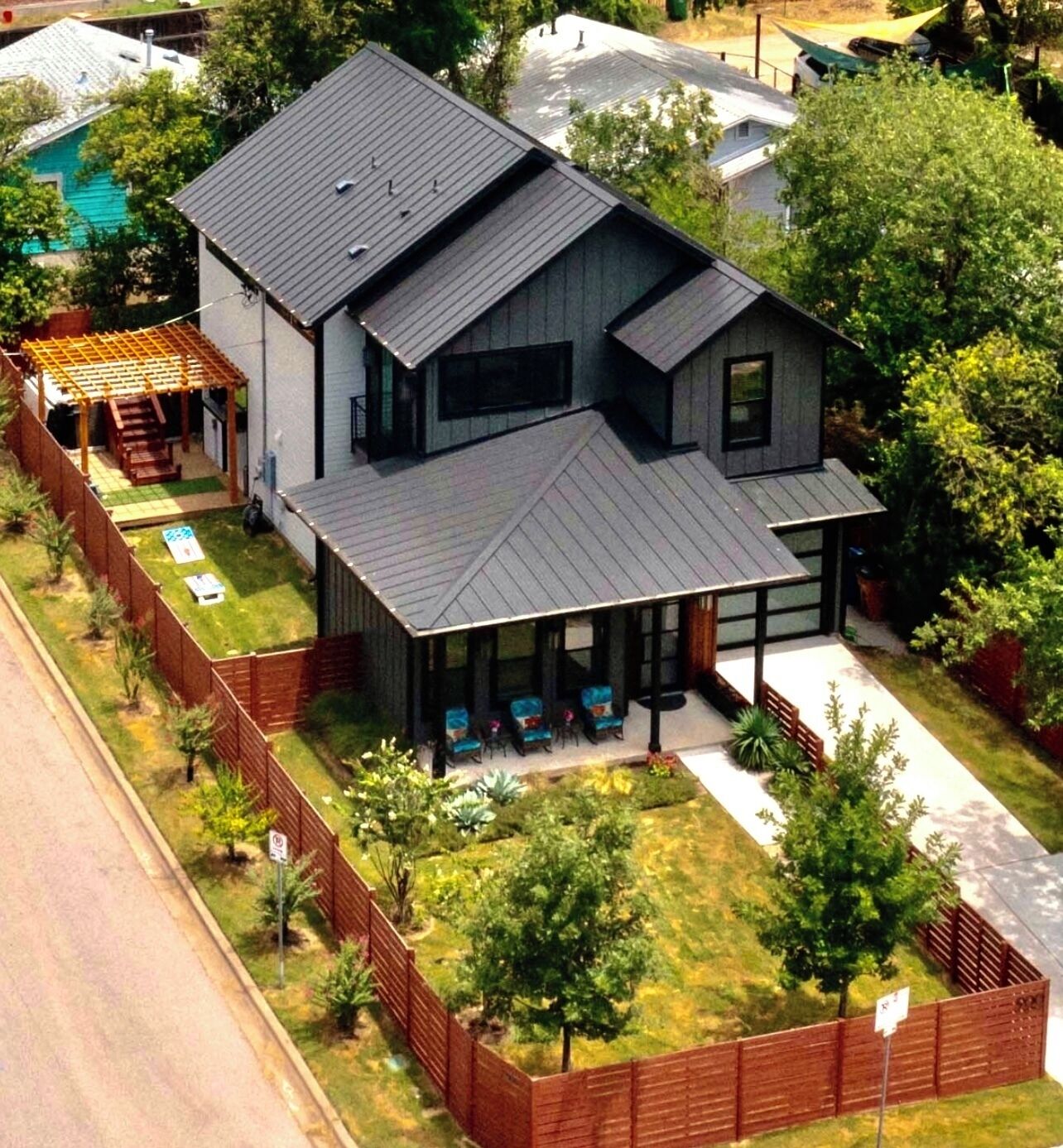 A modern two-story house with a covered patio, a fenced yard, and a swimming pool in the background.