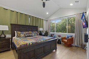 Una camera da letto con un letto grande, un comodino, una sedia, una TV e una finestra con tende.
