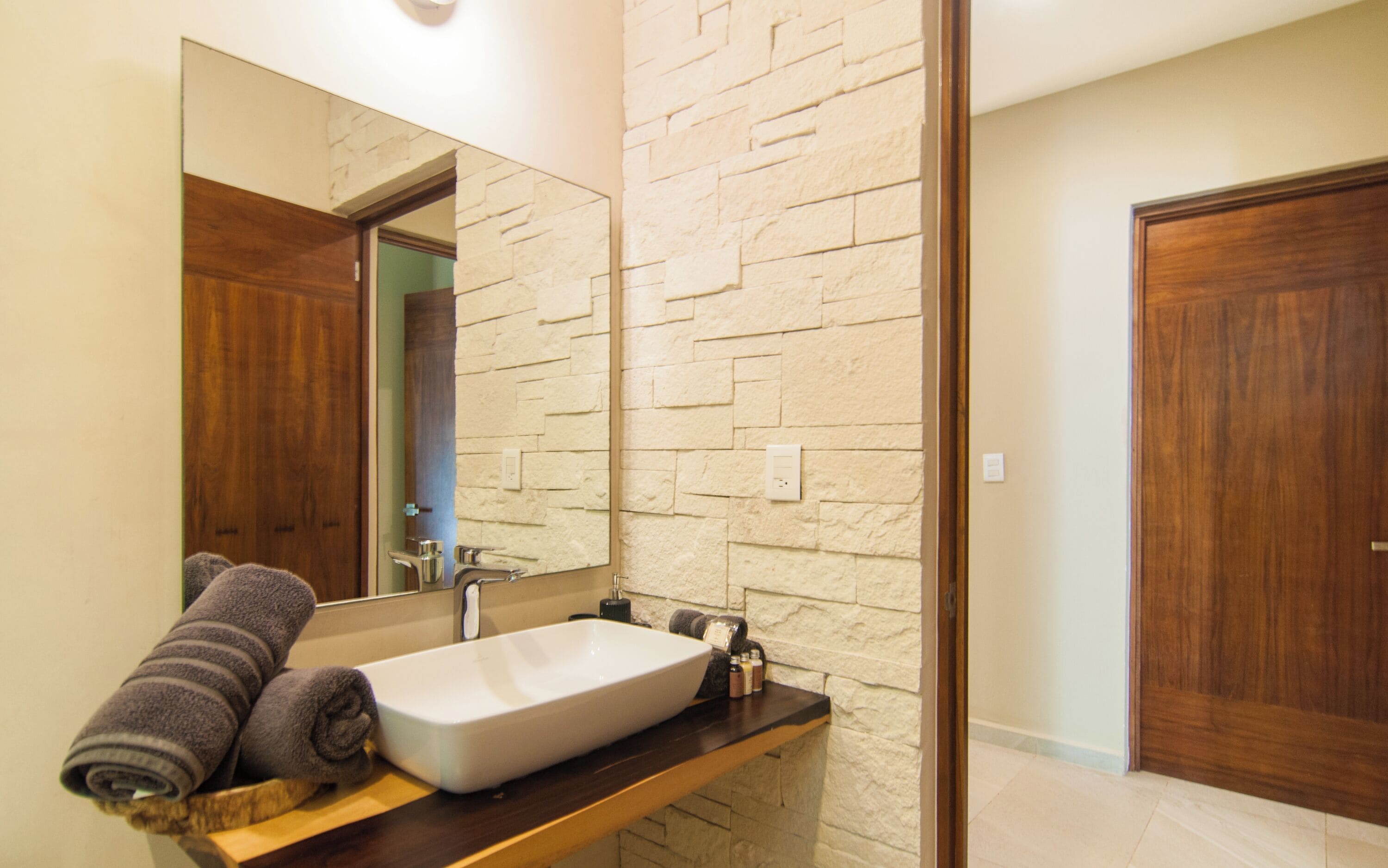 A bathroom with a stone wall, a wooden door, and a sink with a towel on the counter.
