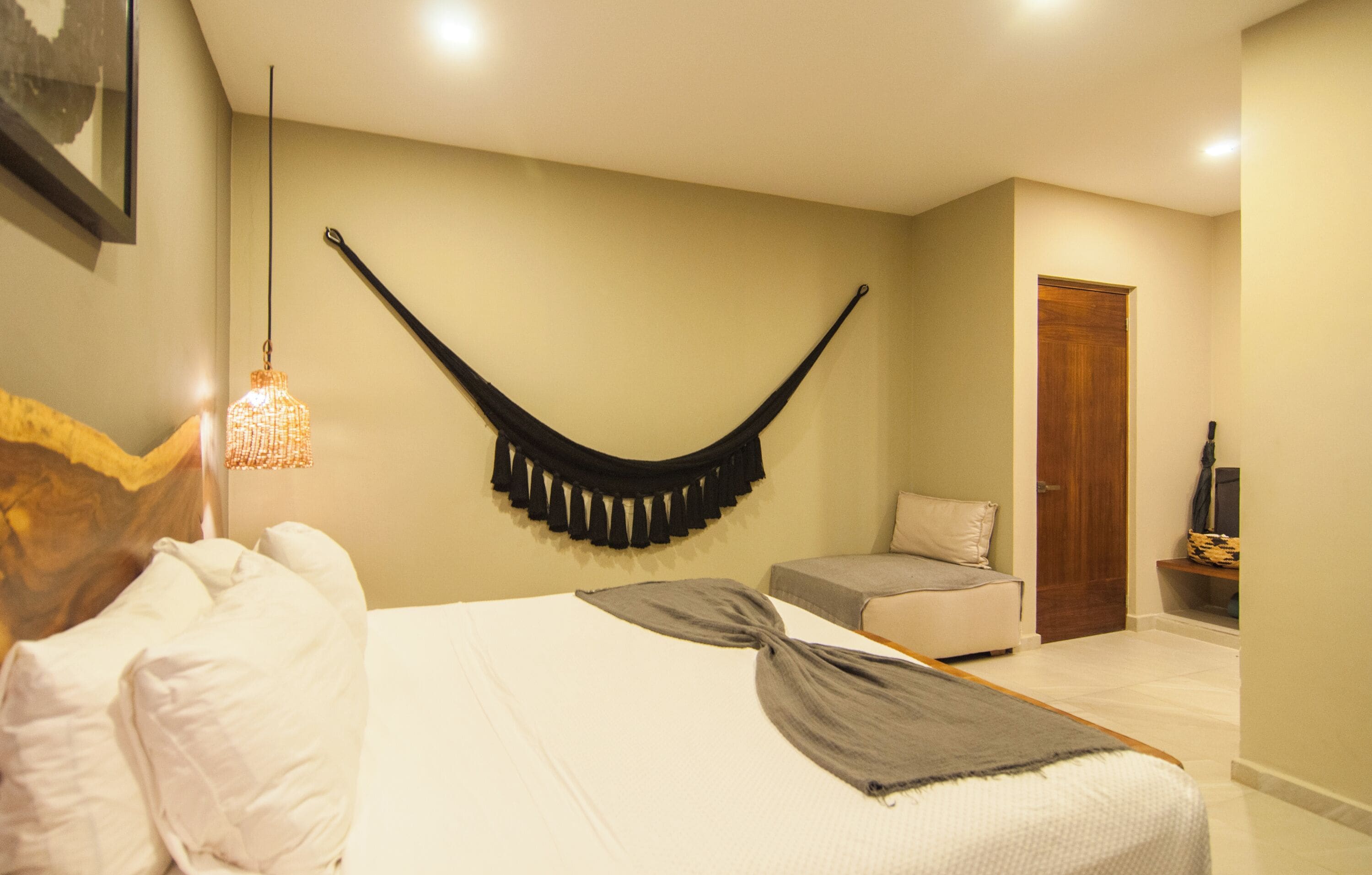 A bedroom with a bed, a hanging chair, a wooden door, and a small shelf with a vase.