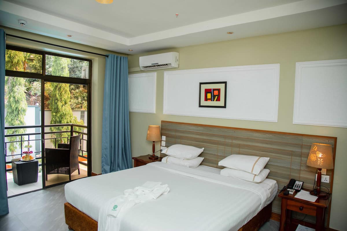 A hotel room with a large bed, two bedside tables, a wall-mounted air conditioner, and a balcony with a chair and table.