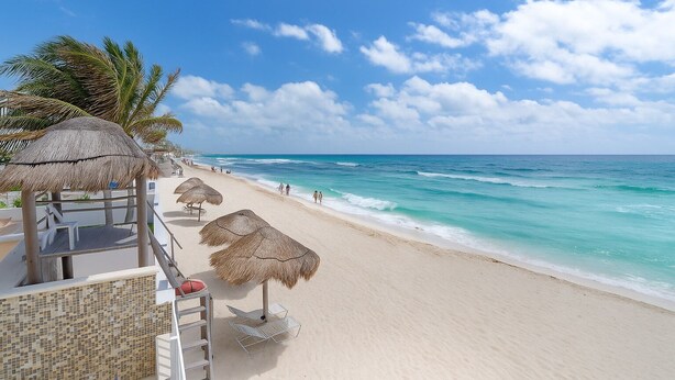 Ein Strand mit reetgedeckten Sonnenschirmen, einer Holzterrasse und Blick auf das Meer.