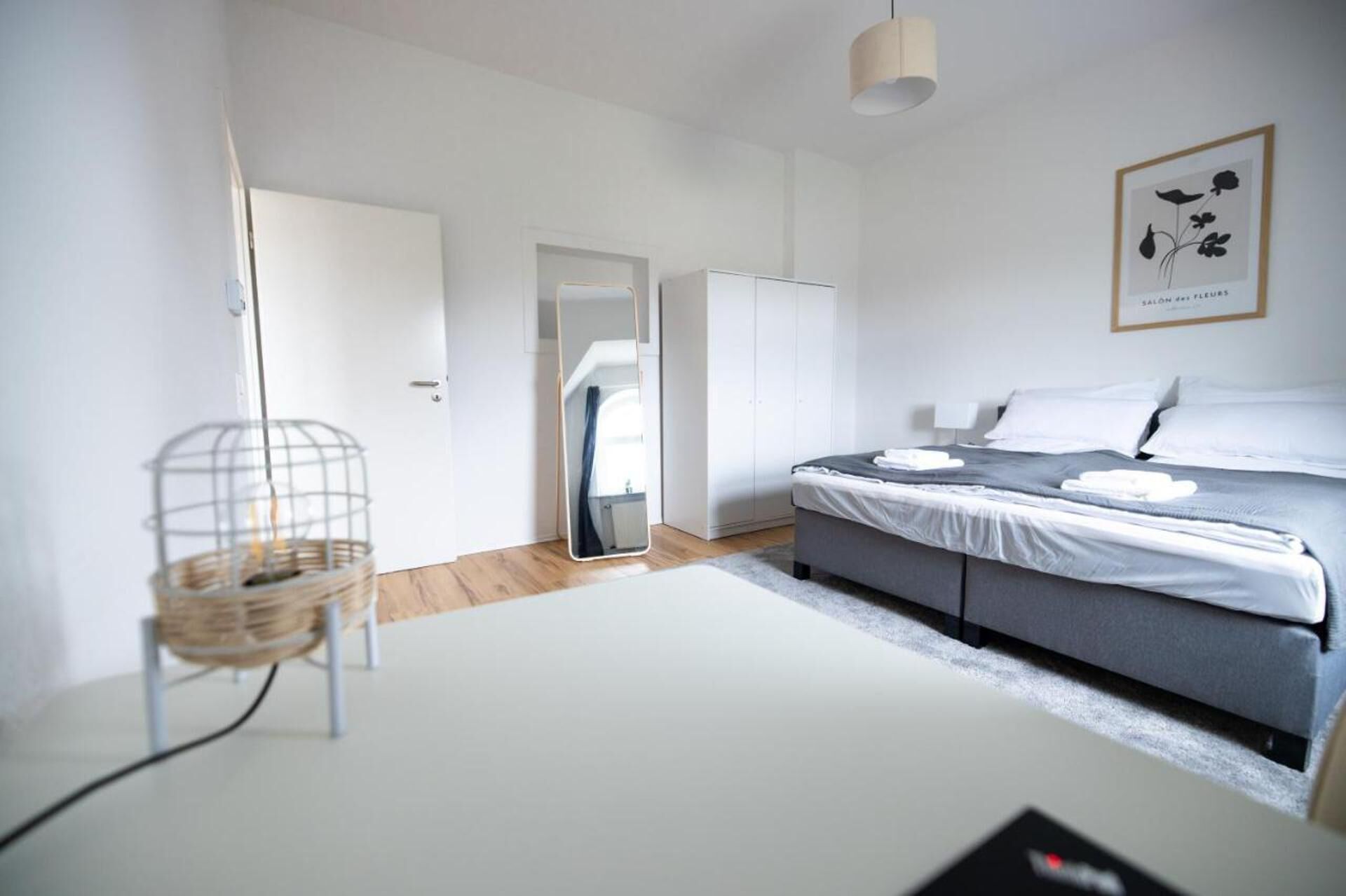 A modern bedroom with a bed, a wardrobe, a mirror, and a framed picture on the wall.