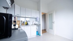 Uma cozinha moderna com armários brancos, bancada com utensílios de cozinha e uma porta que dá para outro cômodo.