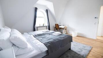 A modern bedroom with a large bed, a desk, and a window with curtains.