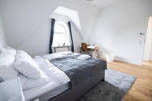 A modern bedroom with a large bed, a desk, and a window with curtains.