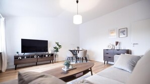 Uma sala moderna com televisão de tela plana, um sofá, uma mesa de centro, uma área de jantar com cadeiras e um aparador.