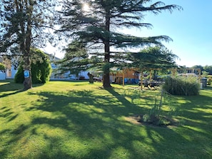 Un área verde bien cuidada con árboles y una estructura de madera, posiblemente un pabellón, en un entorno residencial.